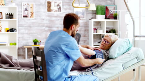 in retirement home male nurse checks old sick lady blood pressure