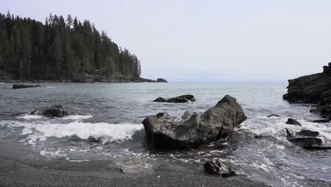 slow motion of foamy sea waves hitting rocky shore, woodland in background on an overcast day, sombrio beach, british columbia, canada