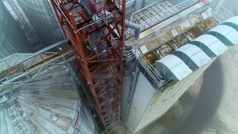 metal supports near the huge elevator cisterns. going down along the tower standing between the warehouse and grain tank. aerial view.