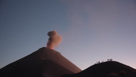 cinematic eruption at fuego volcano: silhouetted group on ridge, ash, lava, and tourists, vibrant sunset hues