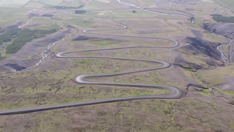 Winding-dirt-road-with-hairpin-corners-going-up-mountain-side-in-Iceland,-aerial