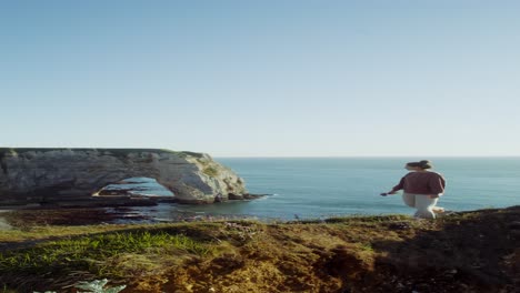 mujer con vistas al océano y un arco costero