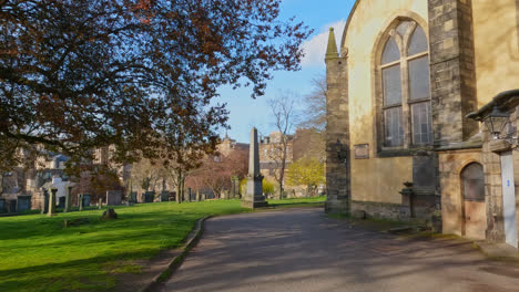 la luz de la mañana se extiende en los antiguos terrenos escénicos de la iglesia de edimburgo, escocia, con árboles sin hojas.