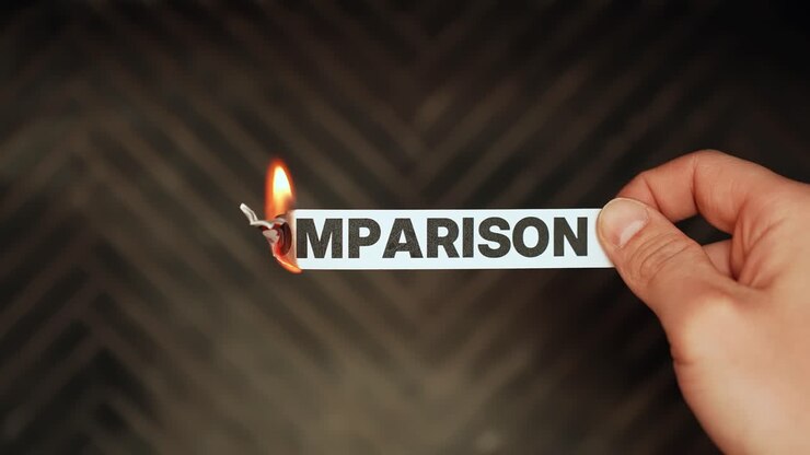 Primer plano de una mano sosteniendo una tira de papel con la palabra “COMPARACIÓN” mientras el borde arde con una llama brillante sobre un fondo oscuro, simbolizando rivalidad, presión en la toma de decisiones y juicio de marketing.
