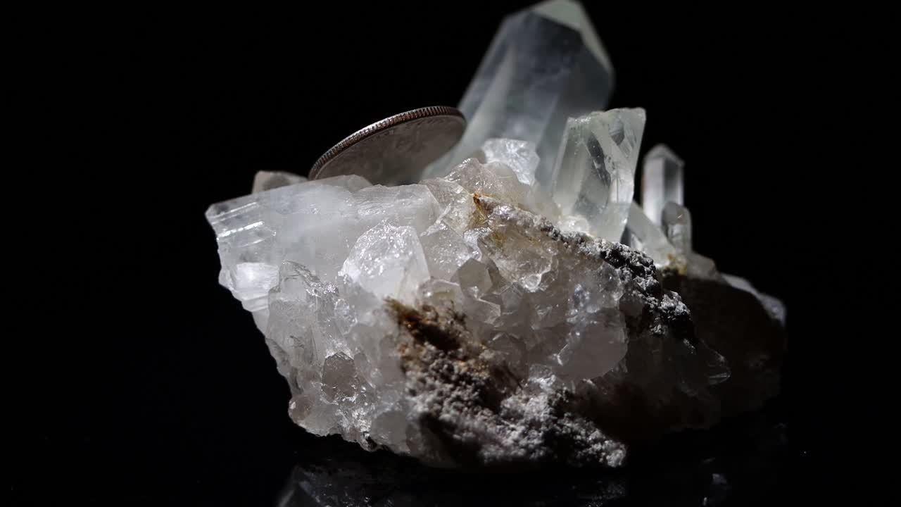 una muestra de mineral de cuarzo con una moneda de diez centavos como referencia de tamaño
