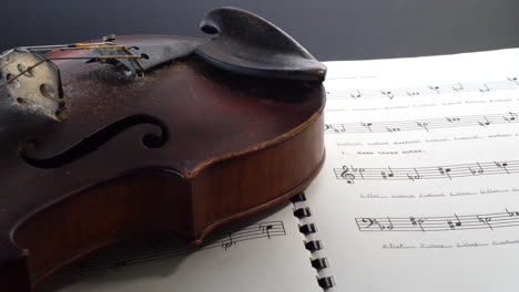 an old dirty vintage violin on top of a notebook full of music lesson homework