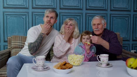 familia multigeneracional mirando la televisión con una niña joven en casa, asustándose viendo una película de terror