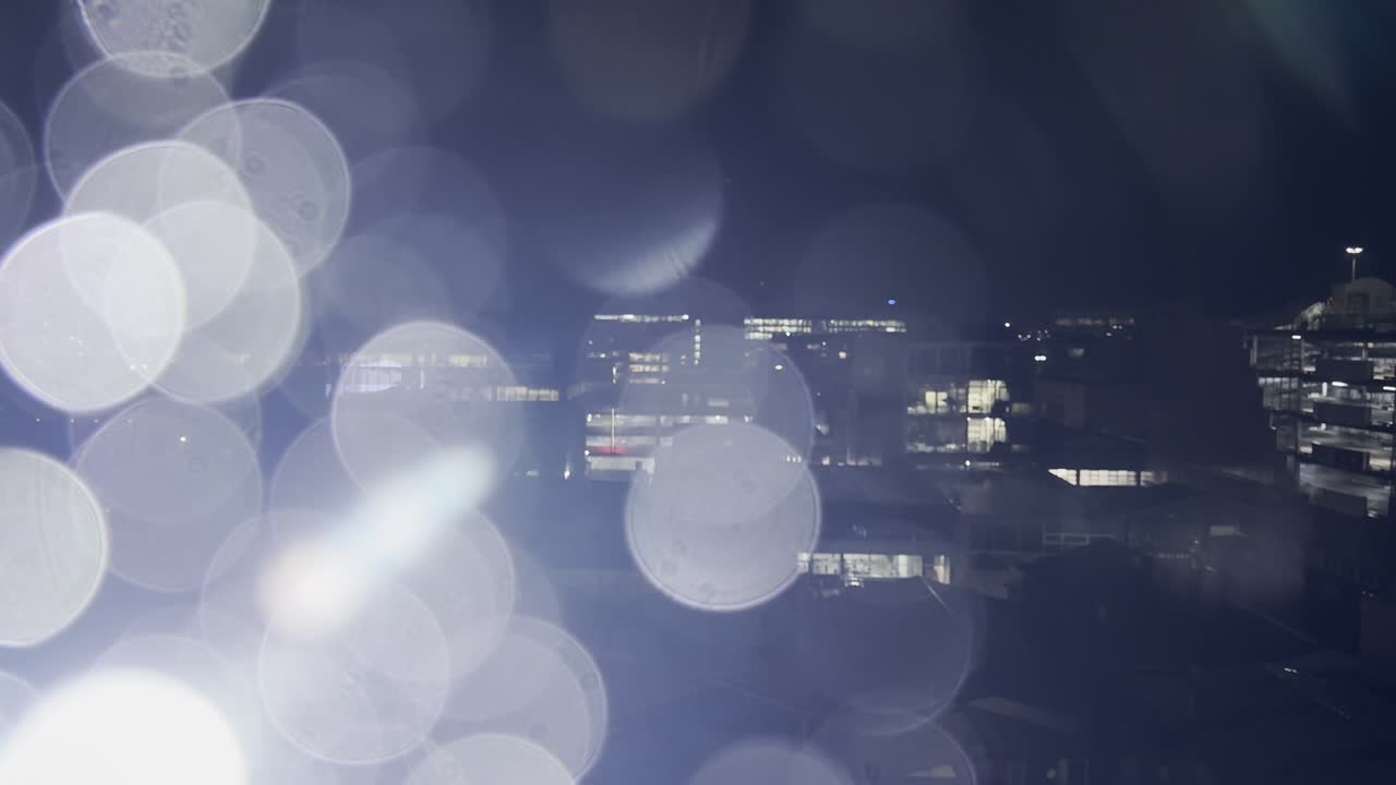 wide shot of city evening buildings and lights with some raindrop falling from the window with light leaks