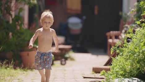 a toddler boy runs happily in the yard on a sunny summer day, his hair swings in the wind