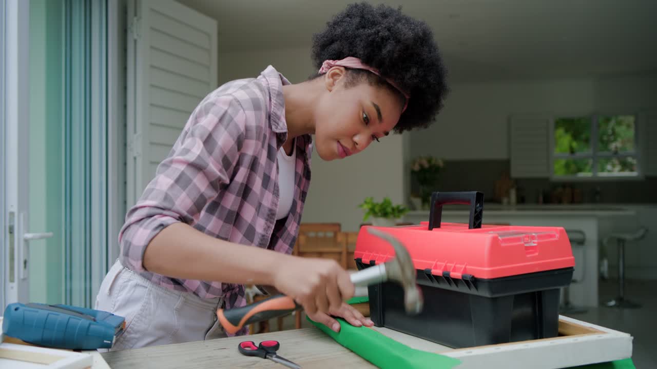 Donna afroamericana che prende la cassetta degli attrezzi, liscia e picchietta su un telaio di legno all'ingresso per fissare il tessuto.
