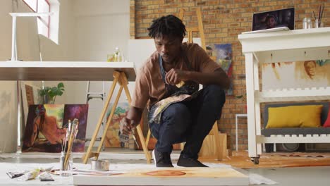 African-american-male-artist-wearing-apron-painting-on-canvas-at-art-studio