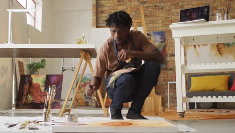 African american male artist wearing apron painting on canvas at art studio