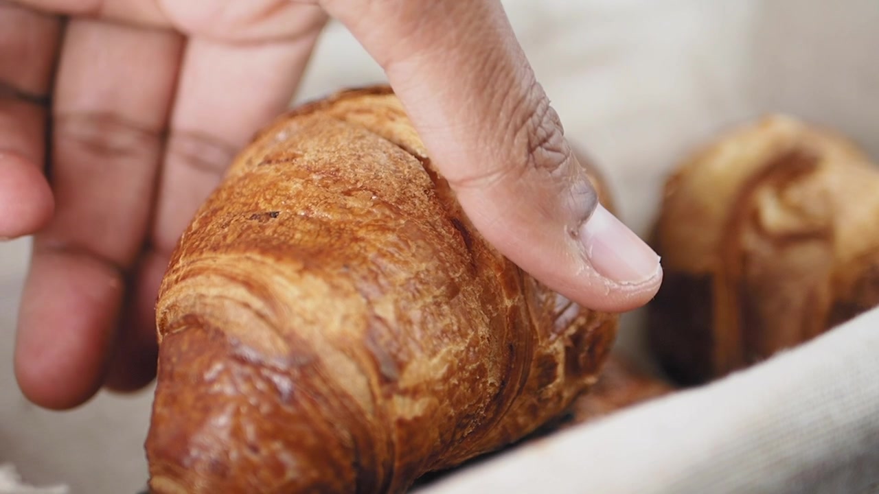 Mano che prende un cornetto fresco da un cestino da panetteria