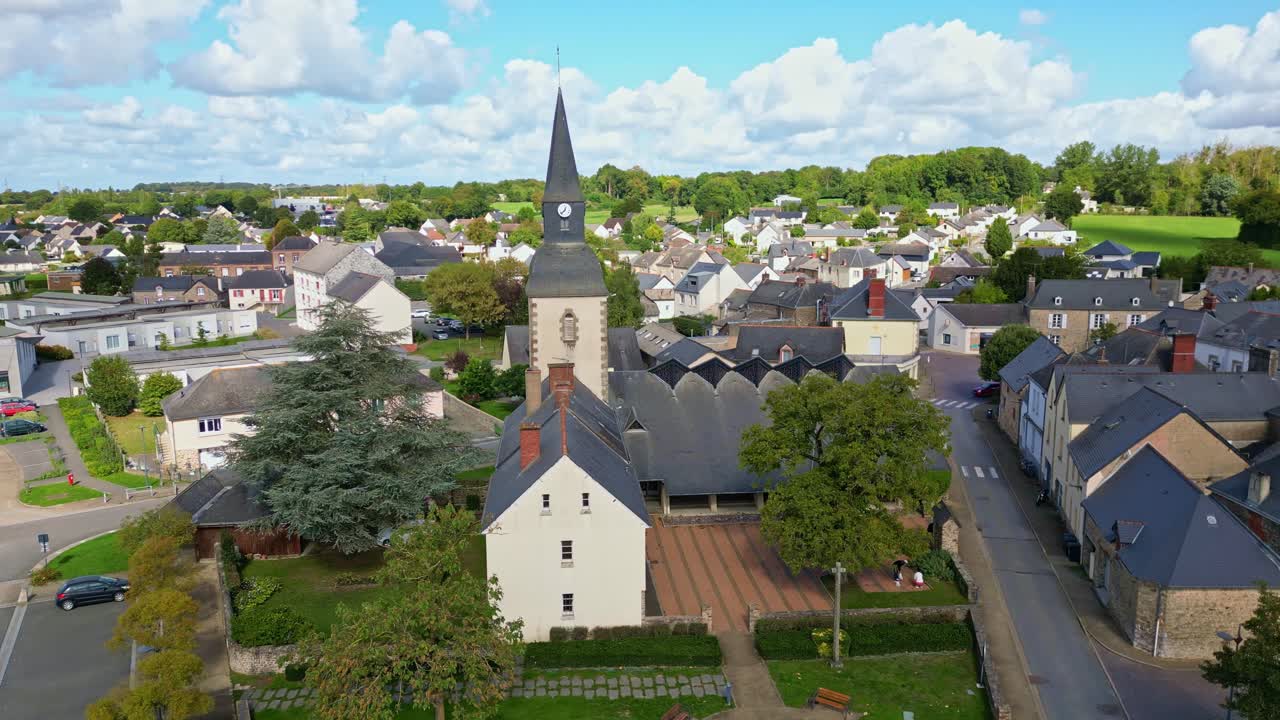 Drone pans around church and town hall in Saint-Pierre-la-Cour, Mayenne, under cloudy sky