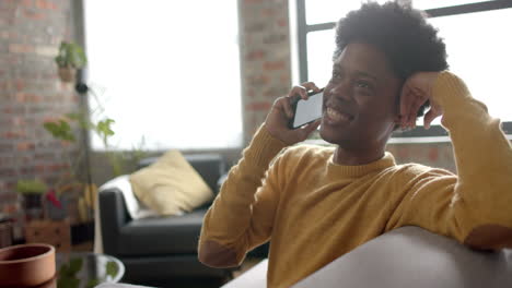 Happy-african-american-man-sitting-on-sofa-talking-on-smartphone-at-home,-slow-motion