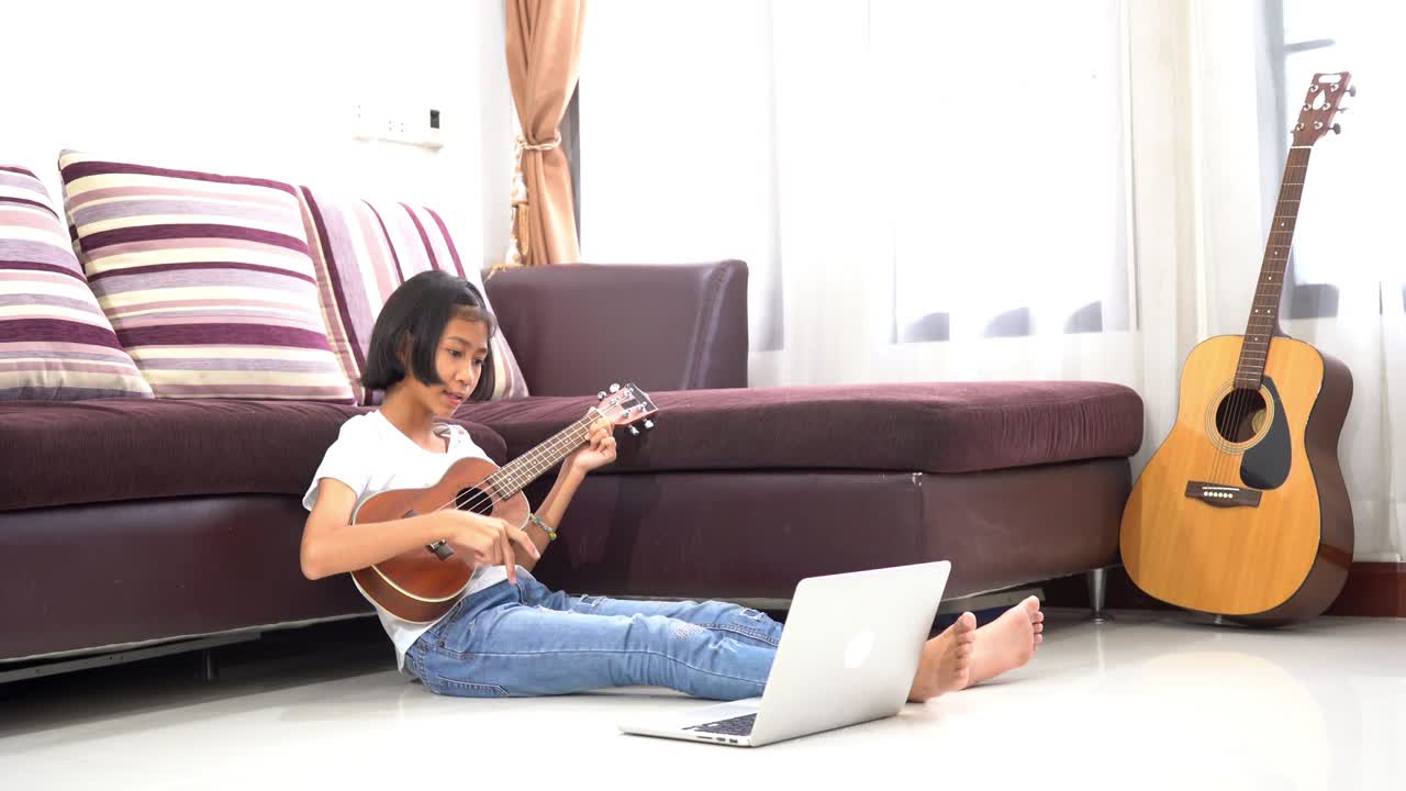 집 에서 노트북 컴퓨터 를 보고 우쿨 을 연주 하는 어린 아이