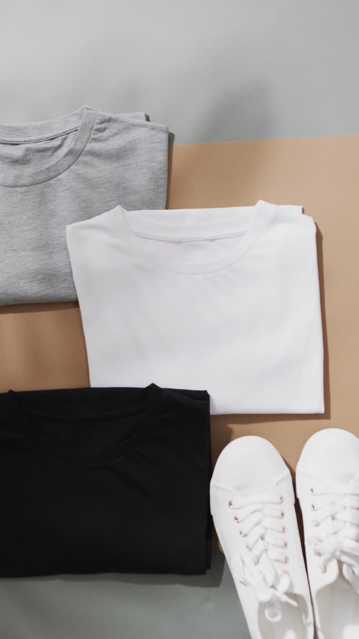 Vertical video of multi coloured t shirts and white sneakers with copy space on grey background