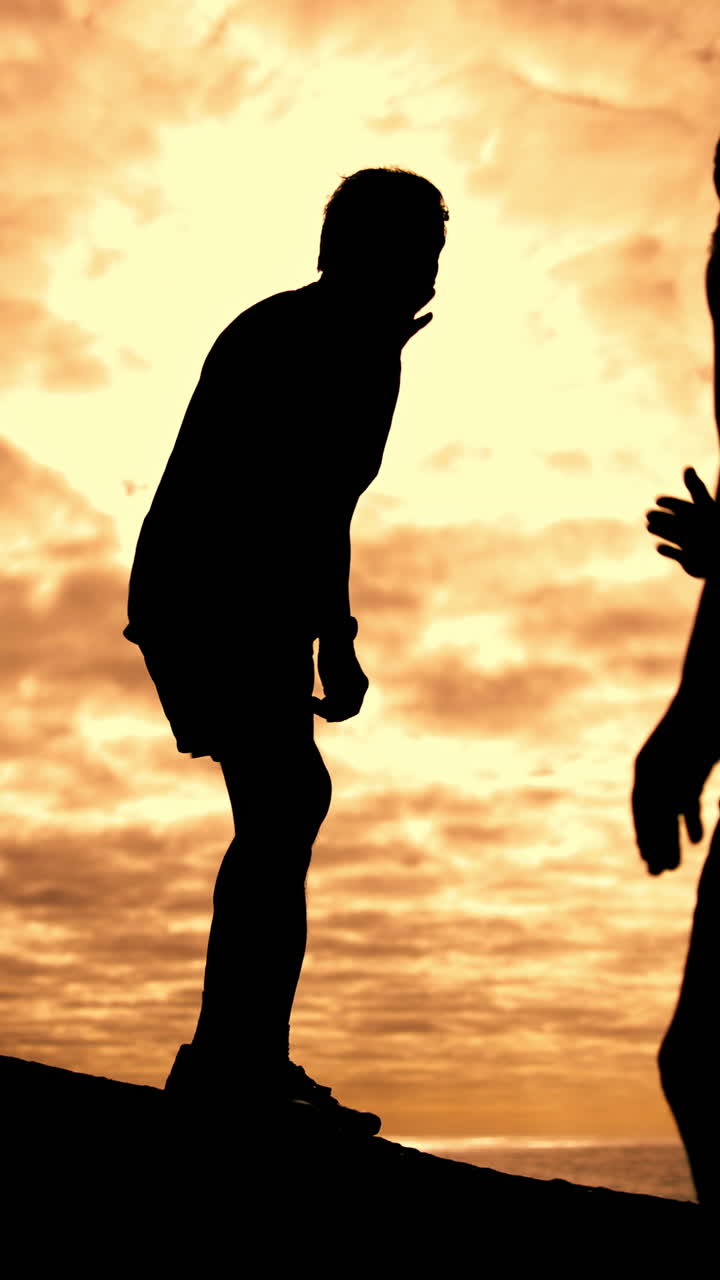 Silhouette di due uomini che si aiutano a vicenda e si danno il cinque al tramonto