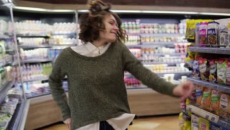 Portrait-of-young-woman-with-shirt-curly-hair-dancing-standing-at-grocery-store-aisle.-Excited-woman-having-fun,-dancing
