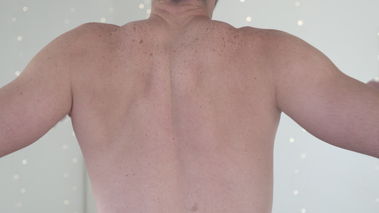 A shirtless man stretching his shoulders and elbows, emphasizing back muscles and neck alignment. Concept of physical fitness, body posture, and health awareness.