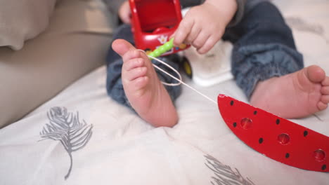 camera focuses on the bare feet of a baby while he is playing with toys on the bed with his mother