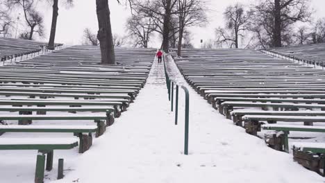 Un-Joven-Con-Una-Capucha-Roja-Y-Pantalones-Negros-Corre-Escaleras-Abajo-En-El-Anfiteatro-En-Invierno