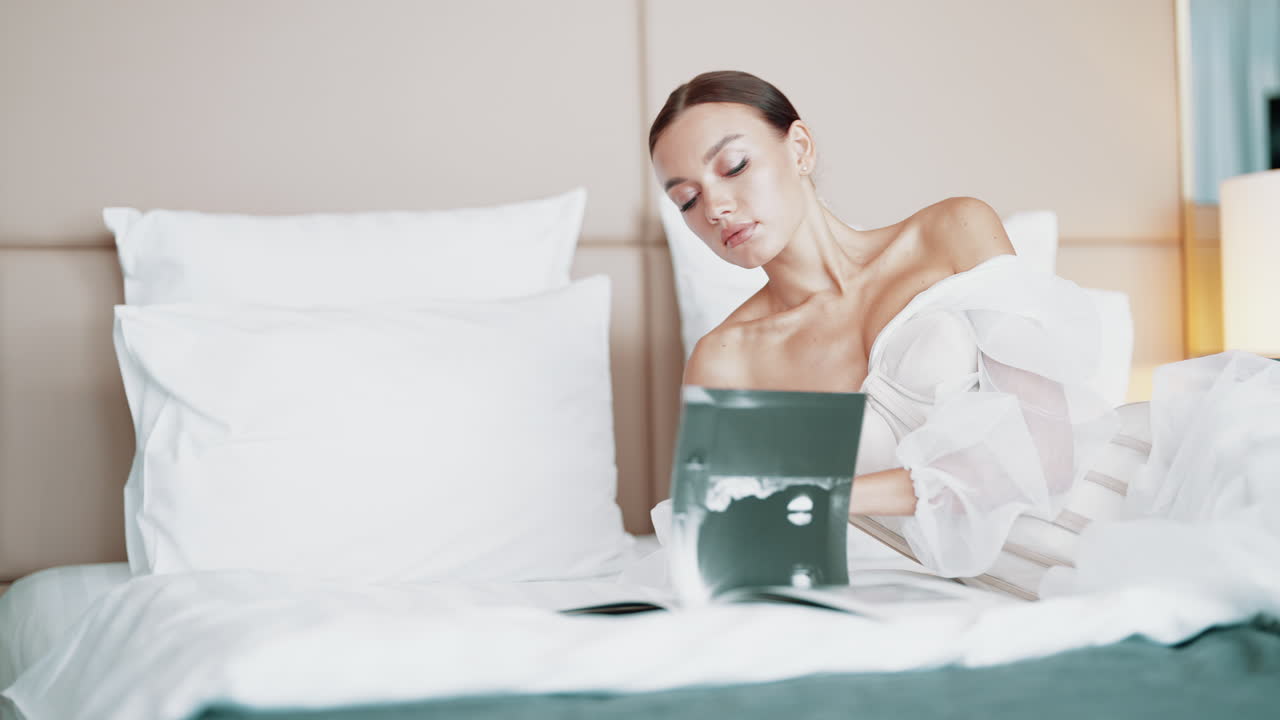 Woman in Elegant White Dress Reading in a Hotel Room