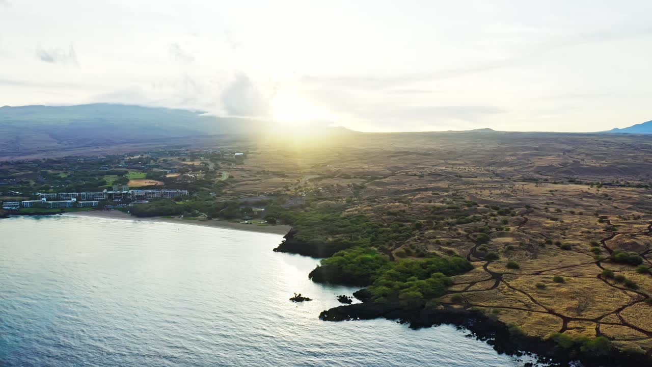 Golden sunlight spills over Hawaii’s volcanic ridges, touching the quiet coastline and shimmering ocean — a serene glimpse of dawn on the island’s wild edge