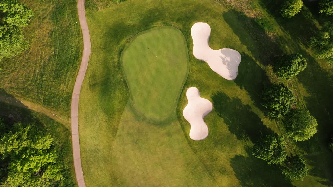 Patterned golf course greens and fairways with sand bunkers viewed from above, drone top down pan