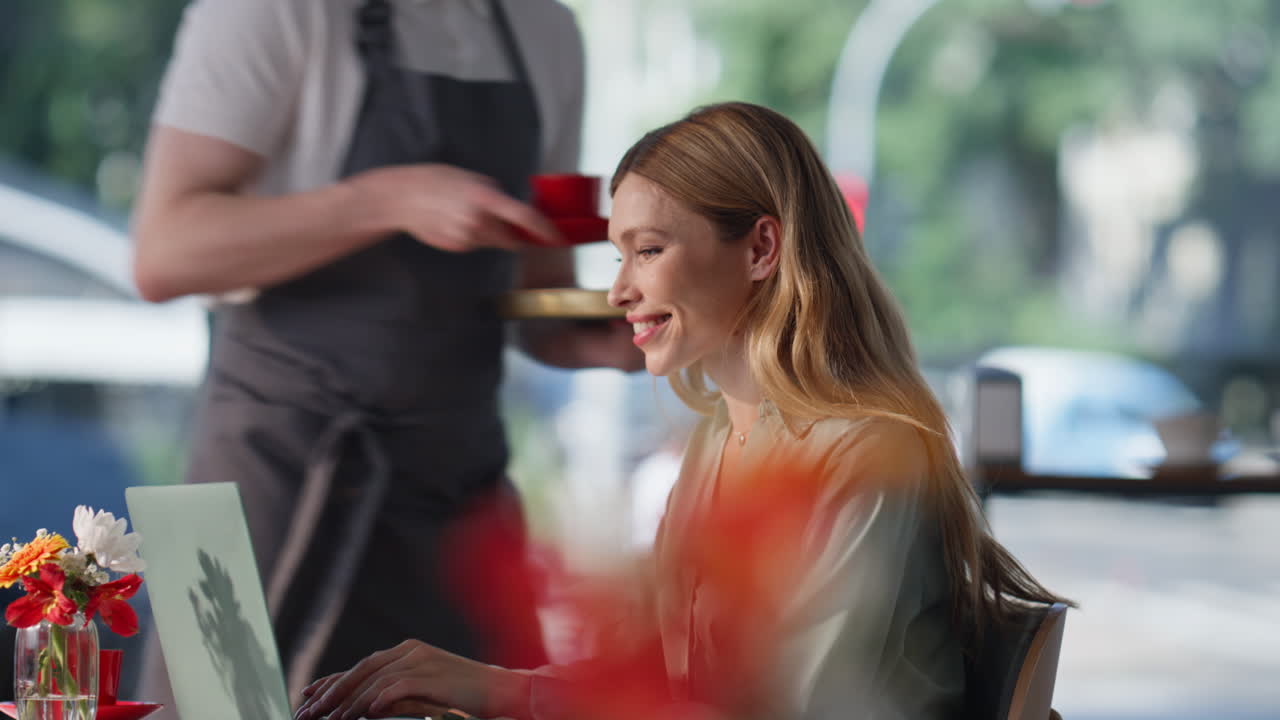 SchriftstellerIn tippt auf Laptop im Restaurant und denkt über die Handlung nach (Nahaufnahme). Kellner bringt Kaffee