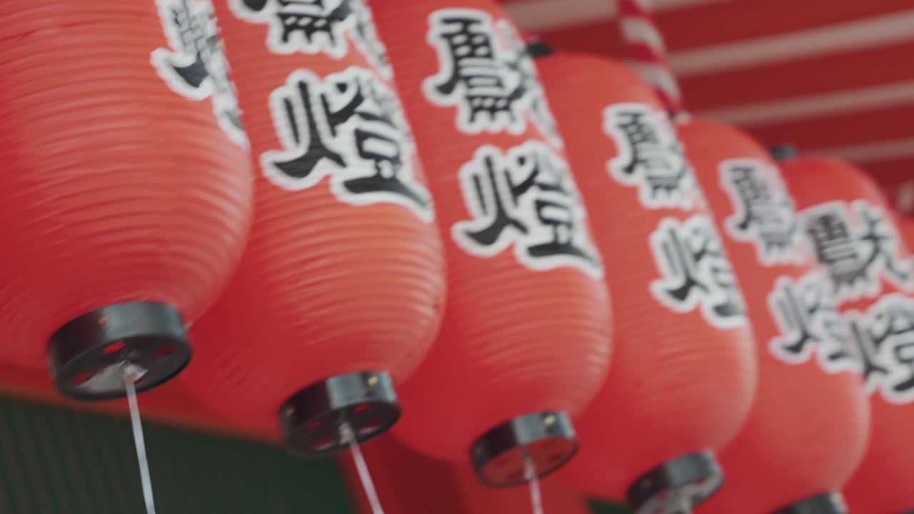 A close-up video capturing the intricate details of glowing red lanterns adorned with Japanese writings at a temple, showcasing the spiritual ambiance and rich cultural heritage of the sacred site.
