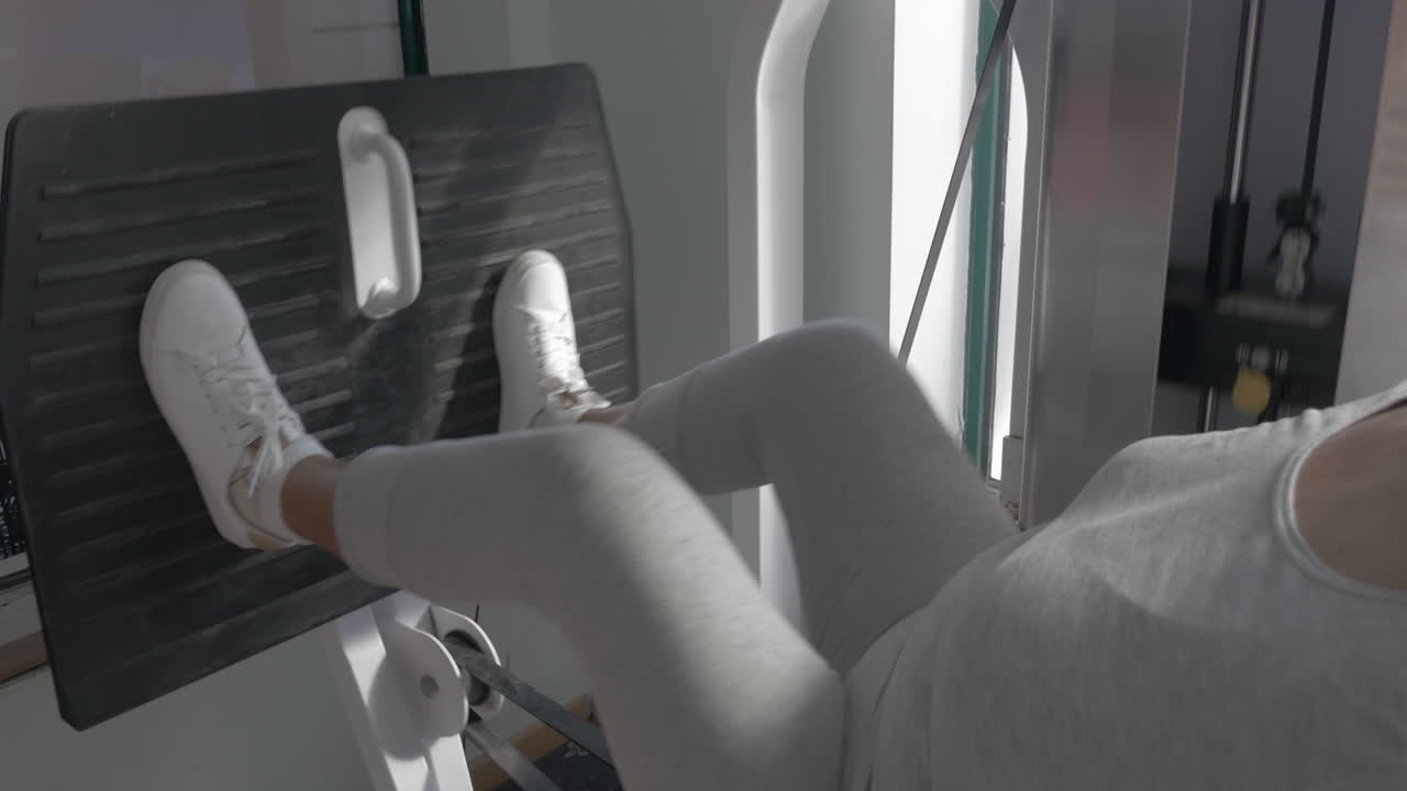 고위 여성이 다리 프레스 기계에서 일하고 있습니다.