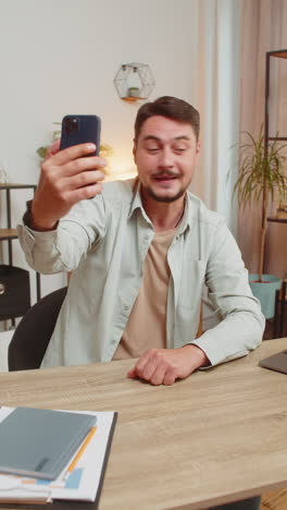 caucasian young man freelancer using smartphone having video call smiling while sitting at table