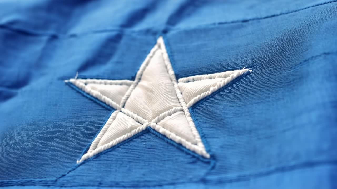 Caméra se rapprochant d'une étoile blanche se déplaçant vers la gauche et remplissant un tissu bleu sur une surface plane, montrant les coutures.
