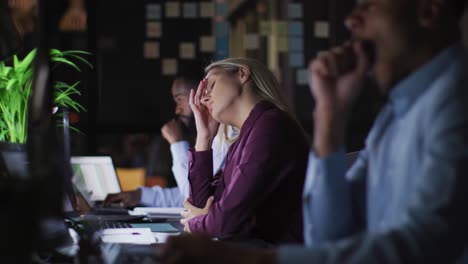 video of tired caucasian busineswoman working at desk at night with colleagues in office