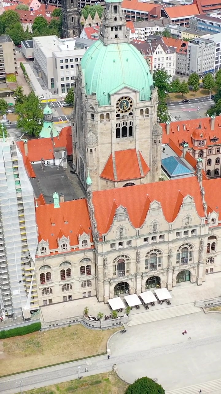 Rekaman drone vertikal sinematik dari Balai Kota Baru Bersejarah Neues Rathaus di Hanover, Jerman, menampilkan kubah hijau ikonik dan atap merahnya.