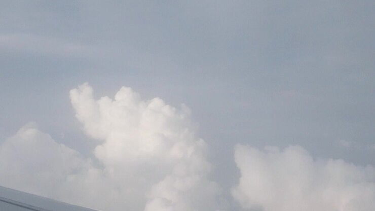 White cumulus clouds rise beneath a pale blue-grey sky, seen from above during air travel