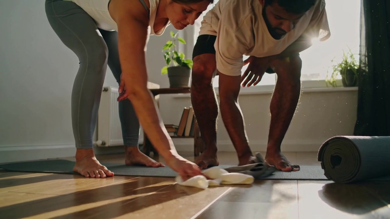 Wiping couple wearing workout clothes at home preparing floor for exercise with cloths and yoga mat