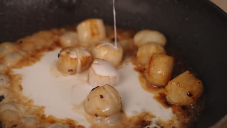 primer plano de cocción del chef agregando leche de coco en una sartén con deliciosas vieiras de marisco fresco burbujeando, dorando y abrazando a fuego alto