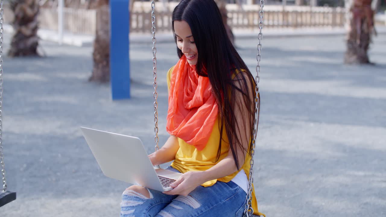 mujer elegante sentada en un columpio con su portátil