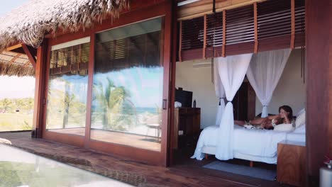 woman and cat relax on a canopy bed in a luxury thatched roof villa with an ocean views