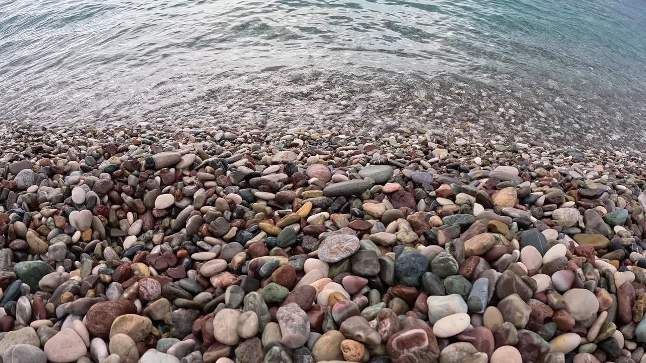 Vista ravvicinata dal basso di ciottoli colorati lungo la battigia con piccole onde che si infrangono sulla spiaggia rocciosa dell'isola di Creta in Grecia.