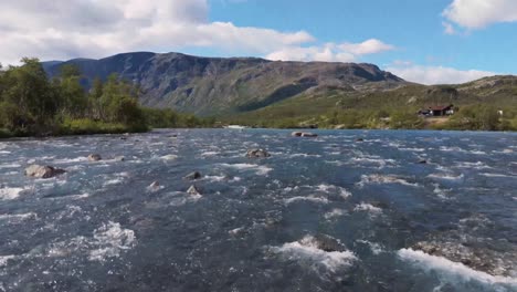 aerial wide shot of a river flowing through a picturesque landscape in norway, surrounded by mountains and lush greenery