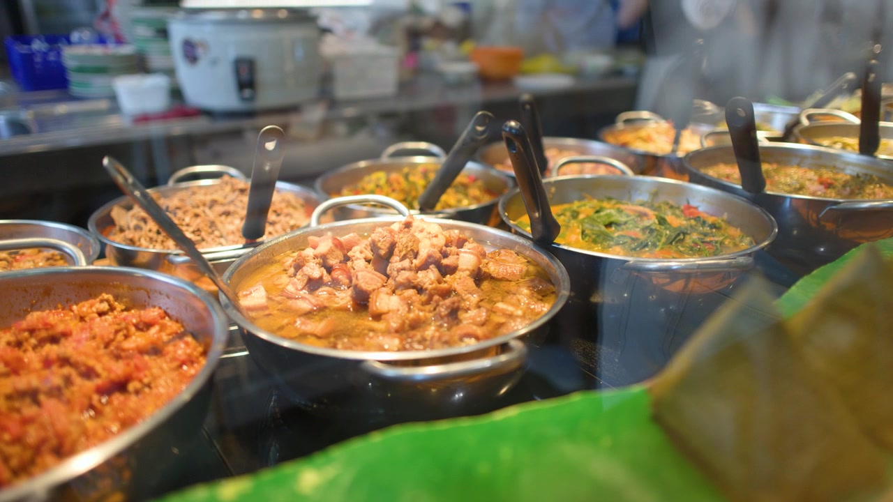 Primo piano di fumanti curry thailandesi e stufati di maiale esposti in un buffet di una caffetteria