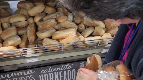 video of a person in a bakery picking out which breads to buy from a big pile and putting them into a bag