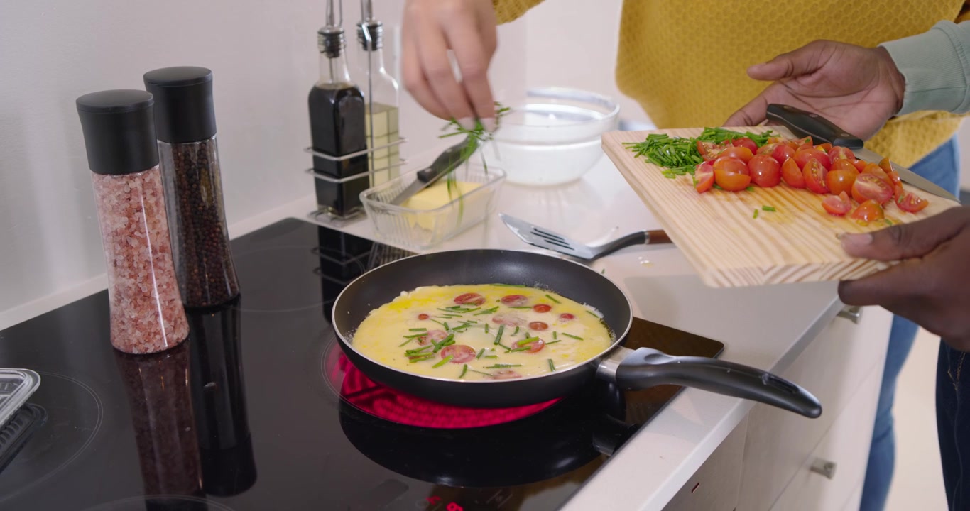 Pasangan Afrika memasak di dekat kompor yang sangat panas, menambahkan tomat dan rempah-rempah ke telur, menyiapkan omelet.