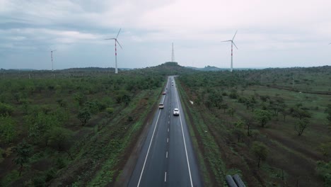 Vista-Aérea-De-La-Carretera-Recta-Con-Conducción-De-Automóviles-En-Un-Parque-De-Turbinas-Eólicas-Para-El-Suministro-De-Energía-Verde-Renovable-Eléctrica