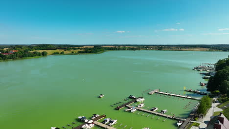 Aerial-shot-of-the-expansive-green-lake-in-Ryn,-Warmia-Masuria,-with-a-marina-and-surrounding-countryside