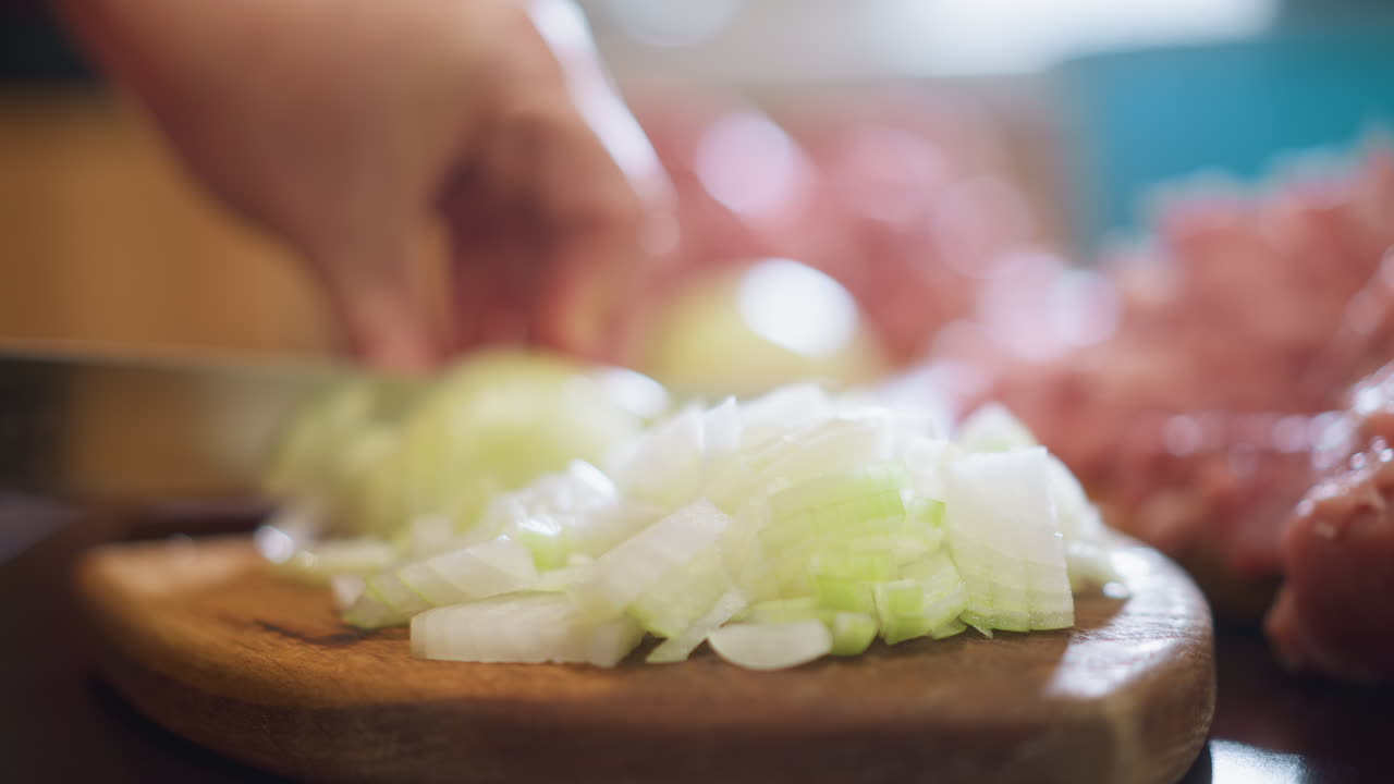 Home kitchen closeup chopping onion board, hands slicing green onion on wooden cutting board, raw pork mound blurred in background, warm natural light, shallow depth of field, comforting homestyle