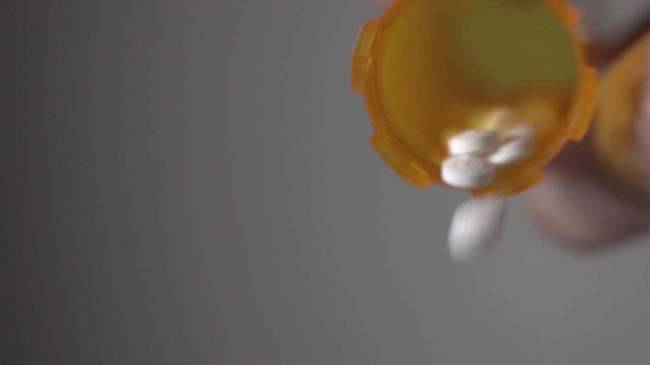 White Round Tablets Falling From A Yellow Plastic Bottle Against Gray Isolated Background - Closeup Shot